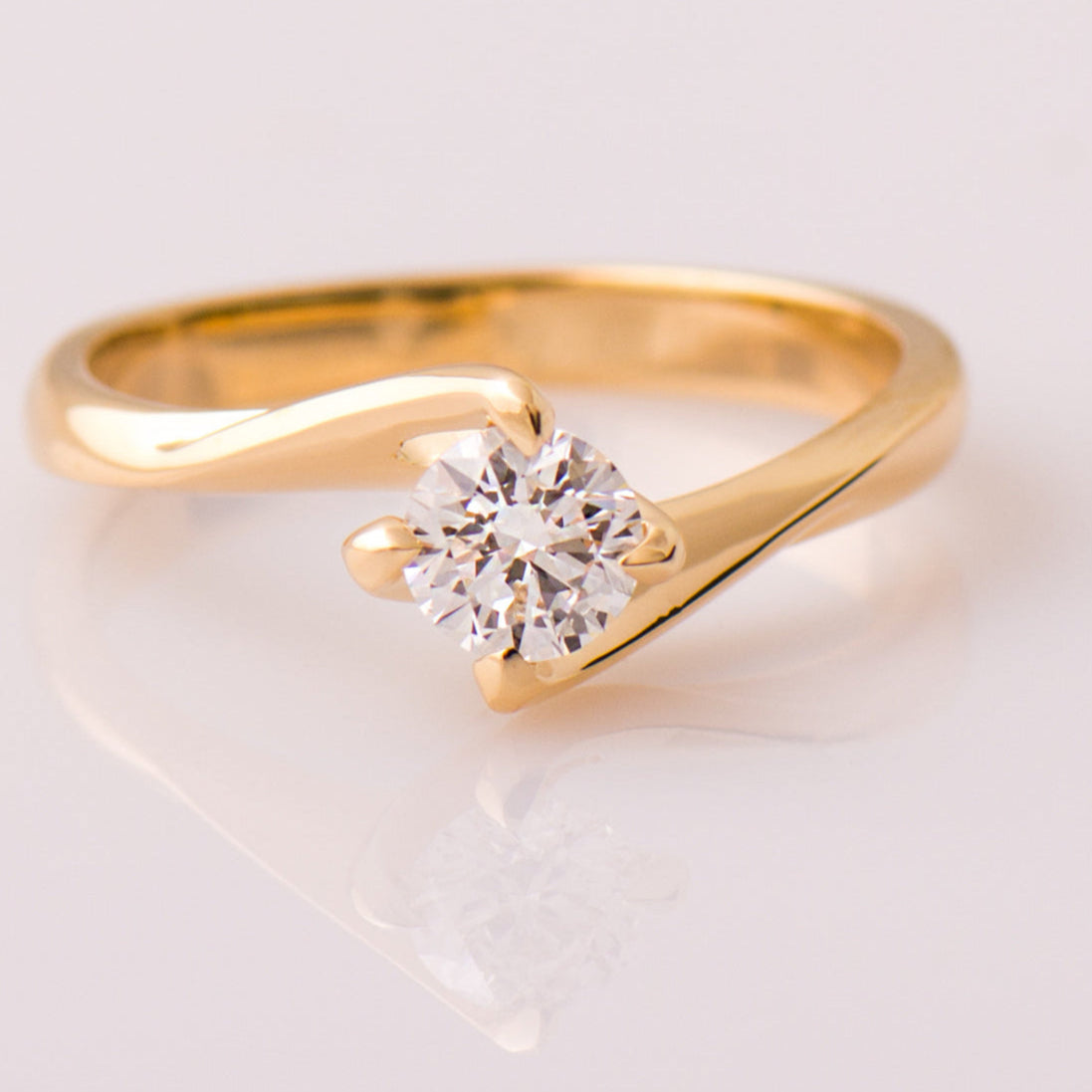 A twisted solitaire engagement ring with a round clear diamond, set in a gold band.